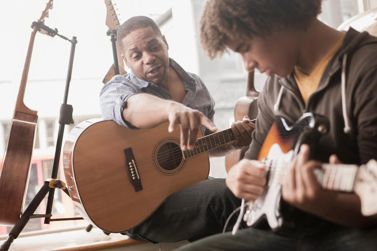 Guitar coach helping his student learn to play the guitar.' title='You can be a coach (or hire a coach) at Dash Class.